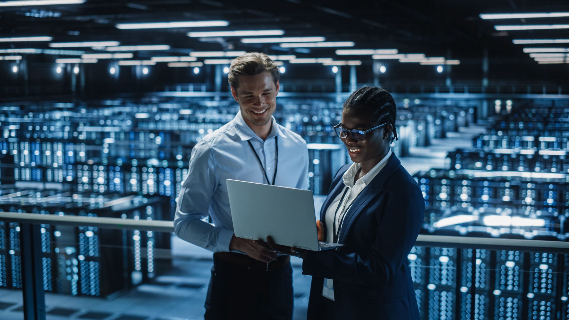 Deux personnes debout dans un centre de données qui regardent un ordinateur portable en souriant.